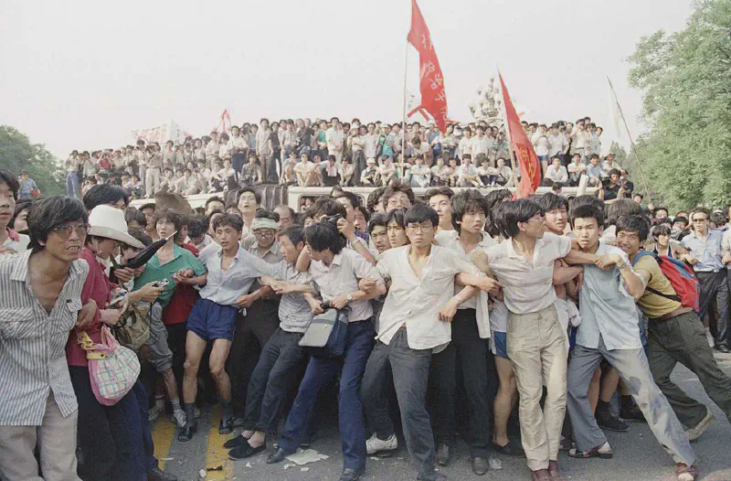 Pro-democracy protesters link arms to hold back angry crowds, preventing them from chasing a retreating group of soldiers near the Great Hall of the People, on June 3, 1989 in Beijing. Protesters were angered by an earlier attack upon students and citizens using tear gas and truncheons. People in the background stand atop buses used as a roadblock. AP Photo/Mark Avary