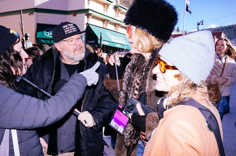 A cluster of festivalgoers in conversation on Main Street, phones and selfie sticks in hand.