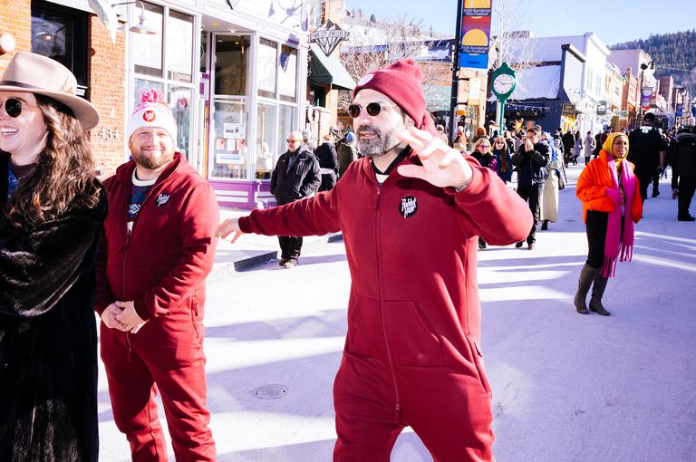 Two men in matching maroon onesies pose for the camera on Main Street, one flashing a peace sign.