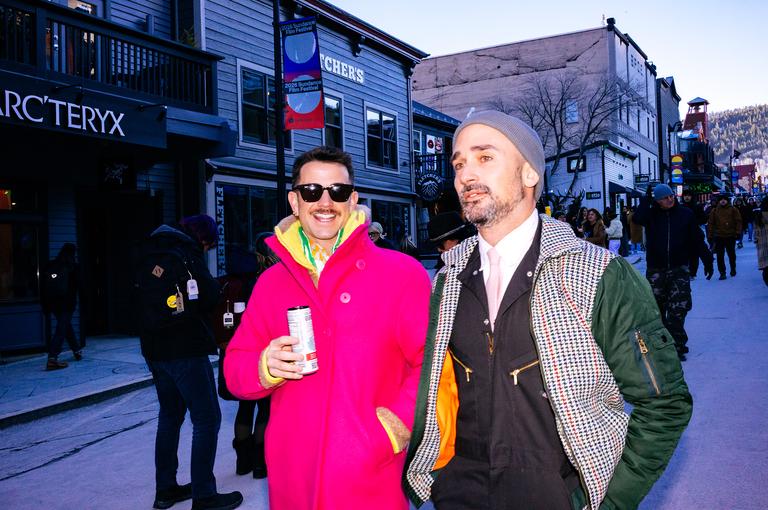 Two men outside the Arc&rsquo;teryx store on Main Street, one in a hot pink ski jacket holding a drink, the other in a houndstooth blazer and grey beanie.