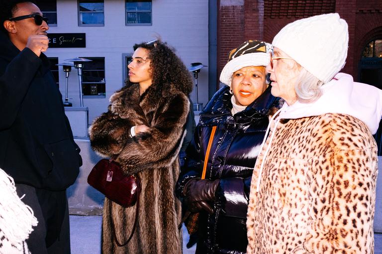 A group of four people standing together on Main Street in winter coats and sunglasses, the afternoon light catching them from the side.