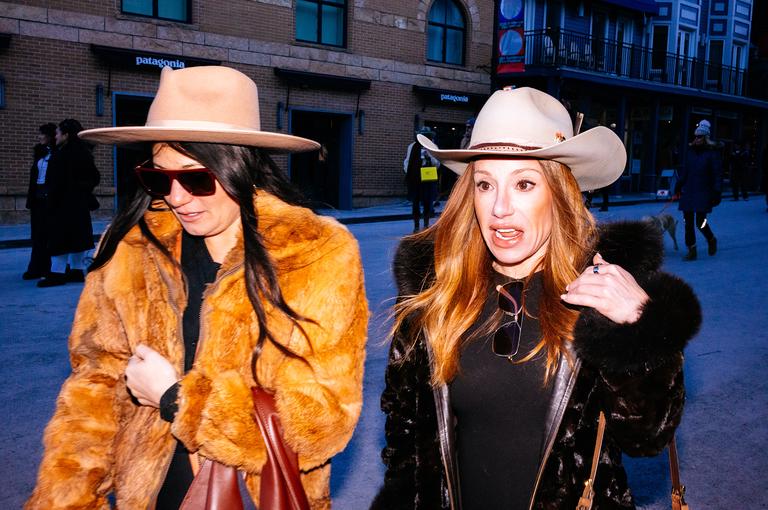 Two women in cowboy hats and fur coats walk past the Patagonia store on Main Street at dusk.